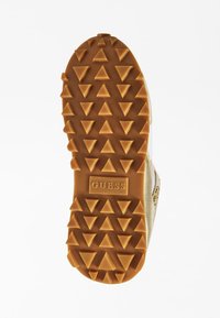 Schuhe mit einer strukturierten Gummisohle, die über dreieckige Profilierungen verfügt, goldenen Akzenten an den Seiten und dem eingeprägten "GUESS"-Logo an der Ferse.