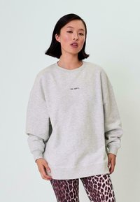 Světlé šedé oversized mikině s dlouhými rukávy a kulatým výstřihem, na přední straně s černým výšivkou "OH APRIL".