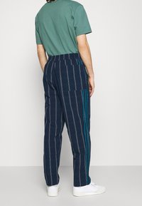 Navy striped pants with a relaxed fit, featuring vertical lines and teal accents, paired with a green crew neck t-shirt and white sneakers.