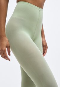 Λεπτό πράσινο κολάν από ελαστικό, υφασμάτινο ύφασμα με υψηλή μέση και σχεδιασμό χωρίς ραφές. Λείο φινίρισμα και εφαρμοστή γραμμή.