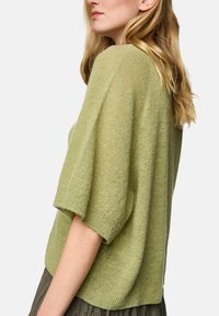 Light green knitted sweater with short sleeves, ribbed cuffs, and a relaxed fit. Soft texture and side slit details enhance comfort.