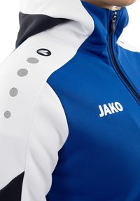 Giacca sportiva blu e bianca caratterizzata da un alto colletto, tessuto testurizzato, dettaglio con logo sulla spalla sinistra e accenti a motivo circolare.