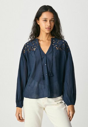 Camicia button-up blu navy in tessuto leggero, con dettagli intagliati intricati sulle spalle e due nappe decorative sul collo.