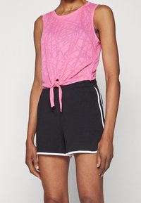 Top sin mangas rosa con patrón texturizado, anudado a la cintura; combinado con pantalones cortos negros con rayas blancas en los lados y un ajuste relajado.