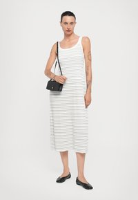 Weiß gestreift Midi-Kleid mit ärmellosem Design, aus einem weichen Stoff gefertigt. Akzentuiert mit einer kleinen schwarzen Umhängetasche und schwarzen Ballerinas.