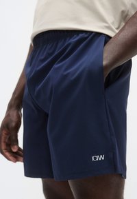 Μπλε αθλητικό σορτς κατασκευασμένο από ελαφρύ ύφασμα με ελαστική μέση. Διαθέτει μικρό λευκό λογότυπο στο κάτω αριστερό μέρος.