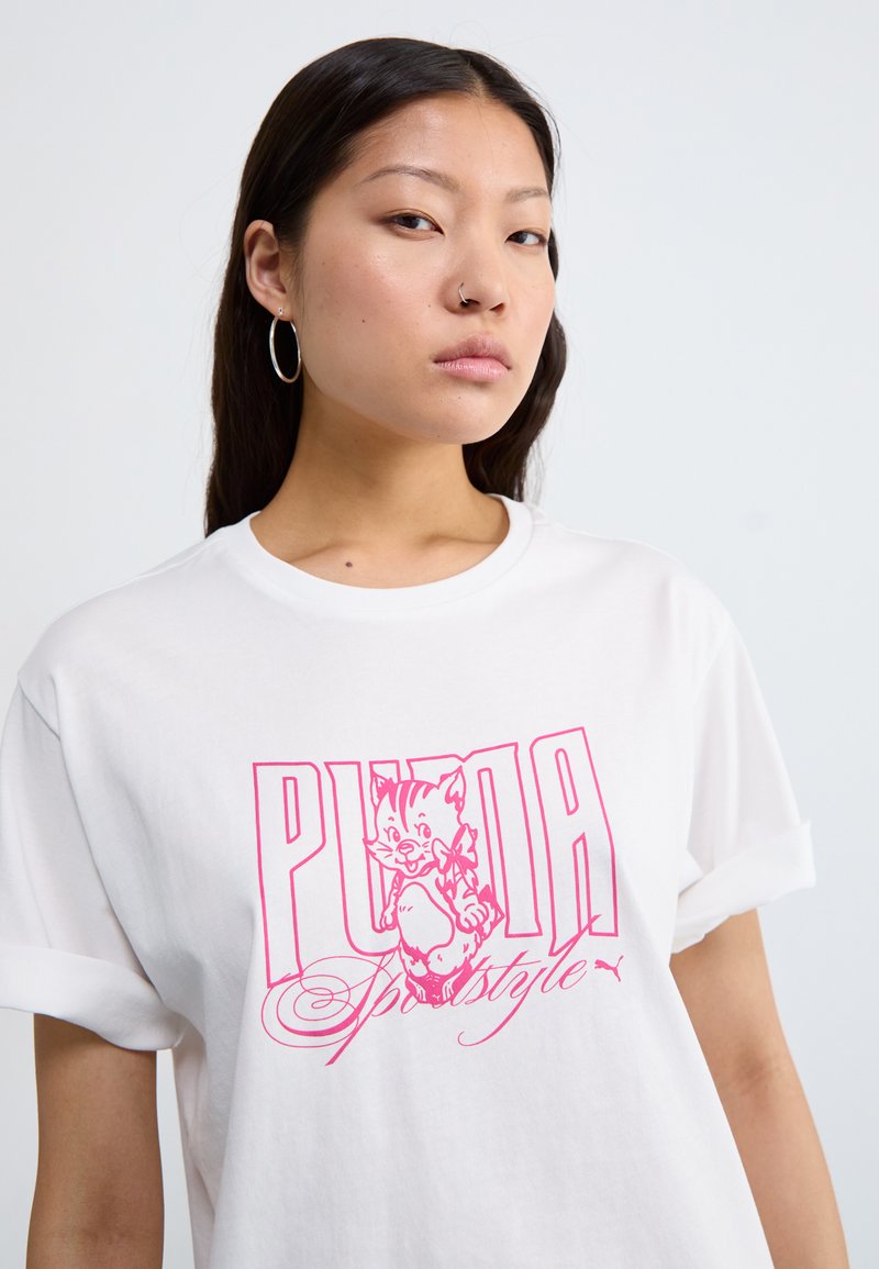 Camiseta blanca con un estampado gráfico rosa de un gato de dibujos animados. Mangas cortas con puños enrollados. El material parece suave, con un corte relajado.