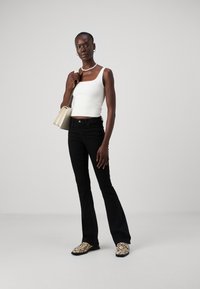 Černé zvonové džíny, přiléhavý bílý crop top a boty s texturou hadí kůže. Doplňky zahrnují malou krémovou kabelku a stříbrné šperky.