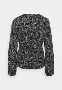 Blouse noire à manches longues avec un motif de cœurs blancs. Taille froncée pour une silhouette ajustée, tissu doux avec une texture lisse.
