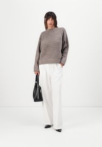 Pull en maille texturée gris avec un col rond, associé à un pantalon large blanc. Le modèle tient un sac à main noir et porte des chaussures à bouts pointus.