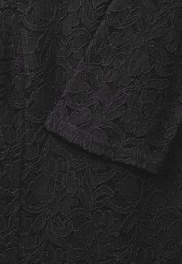 Tessuto di pizzo nero con intricati motivi floreali e una superficie testurizzata. Il design è continuo, mostrando un'apparenza a strati.