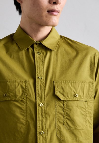Olivno zelena srajca z gumbi iz lahkega materiala, ki ima dva sprednja žepa s poklopcema in kontrastnimi gumbi.