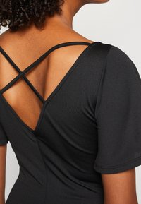 Vêtement noir ajusté avec manches courtes, dos en V profond avec bretelles croisées, et tissu à texture lisse.