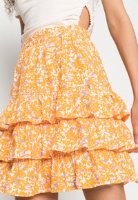 Saia amarelo floral em camadas, com camadas franzidas, padrões de flores brancas e lavanda, e um cós elástico para conforto.