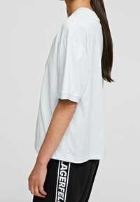 Hellblaues, kurzärmliges T-Shirt mit lockerer Passform, rundem Halsausschnitt und subtilen Textdetails an der Seite, kombiniert mit schwarzen Jogginghosen mit weißem Text.