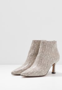 Pointed-toe ankle boots in metallic silver with a textured surface. Features a slim heel and smooth interior lining.