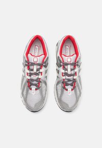 Baskets de course en maille grises avec des accents rouges, des détails blancs et gris, des semelles texturées et un système de laçage traditionnel. Logo de la marque notable sur la languette.