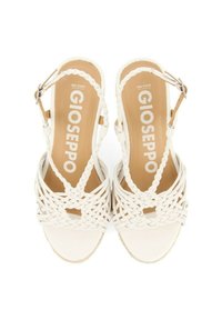 Sandalias de cuña blancas con correas trenzadas, plantilla beige y cierre de hebilla en el tobillo. Textura suave y diseño de punta abierta.