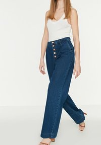 Jeans in denim blu a vita alta con taglio dritto, caratterizzati da bottoni di rame sul davanti e una finitura liscia e texturizzata.