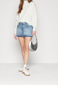 Gonna mini in denim con orlo sfrangiato, colore azzurro chiaro, abbinata a un maglione crema. Una borsa argentata e sneakers bianche completano il look.