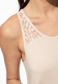 Beiges Tanktop aus glattem Stoff mit Spitze über den Schultern, die ein filigranes Blattmuster zeigt, und einem figurbetonten Schnitt.