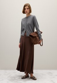 Cardigan grigio lavorato a maglia, vestito di satin marrone, scarpe slip-on nere con decorazioni bianche e borsa a tracolla in suede marrone. Texture morbide e forme semplici.