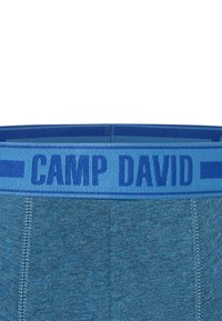 Boxer shorts da uomo blu con tessuto testurizzato. La vita elasticizzata presenta la scritta "CAMP DAVID" in lettere grasse di colore blu scuro su un fondo blu più chiaro.