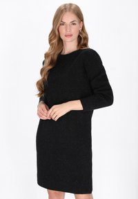 Vestido negro de punto con escote redondo y mangas largas. La tela tiene un acabado texturizado y jaspeado. Termina por encima de las rodillas.