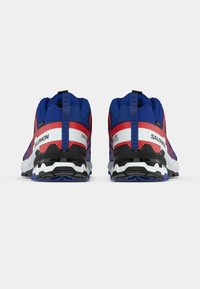 Kék és piros sportcipők texturált felsőrésszel, fekete részletekkel és fehér középtalppal. Jellegzetes hátulján lévő behúzófüllel.
