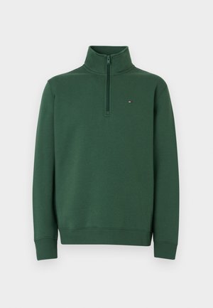 Sudadera verde con cuello alto, cierre de media cremallera, puños acanalados y un pequeño logo en el pecho. Fabricada con tela suave.