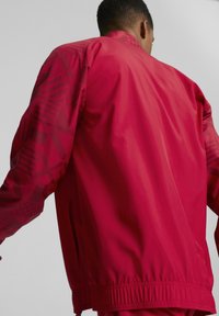 Czerwona, lekka kurtka z geometrycznym wzorem na rękawach, elastycznym pasem w talii oraz zasuwanymi bocznymi kieszeniami dla funkcjonalności.