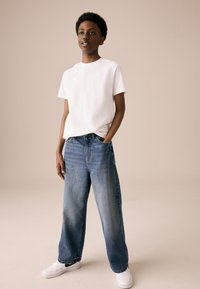 Valge, ümara kaelusega t-särk, mida on kombineeritud siniste, laiade säärega teksade ja valgete spordijalatsitega. Sile kangas, vaba lõige, keskmise tooniga teksad.