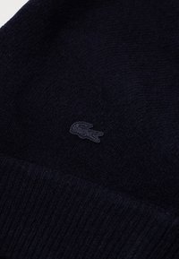 Gorro de punto azul marino hecho de material suave, con un discreto logo bordado. La textura acanalada en el borde agrega detalle.