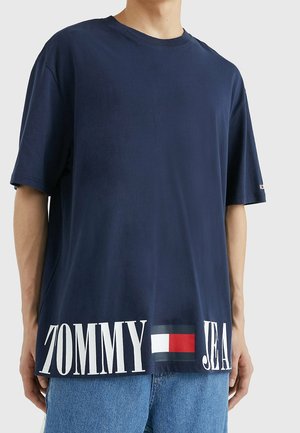 Marineblå bomulds T-shirt med løs pasform, rund halsudskæring og stor hvid tekst "TOMMY" og "JEAN" ved kanten, med en rød, hvid og blå logoaccent.