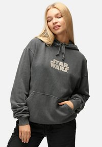 Grå Star Wars-hoodie med känguruficka, dragsko på huvan och mjukt, texturerat tyg. Har en stor, krämfärgad logotyp på framsidan.