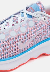 Nike superge s prezračnim mrežastim zgornjim delom v roza in modri barvi, s teksturiranim belim podplatom in okroglimi detajli ob straneh.