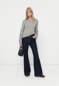 Grå strikket genser med blomsterdetaljer på ermene, sammen med mørke, vide jeans og en strukturert svart håndveske. Flate sko fullfører stilen.