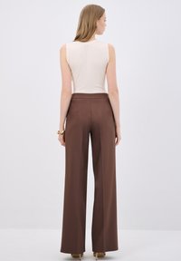 Top beige senza maniche con texture a coste abbinato a pantaloni marroni a gamba larga e a vita alta. Linee semplici e pulite con dettagli minimi.