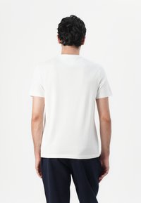 Weißes Baumwoll-T-Shirt mit kurzen Ärmeln und Rundhalsausschnitt. Glatte Textur, schlichtes Design und lockere Passform, von hinten betrachtet.