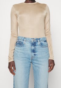 Beige Langarmoberteil mit glatter, glänzender Textur, kombiniert mit hellblauen, hoch geschnittenen Jeans im klassischen Fünf-Taschen-Design.
