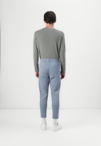 Chemise grise à manches longues, pantalon effilé bleu clair et baskets blanches. Présente une texture lisse avec une coupe décontractée et une taille élastique.