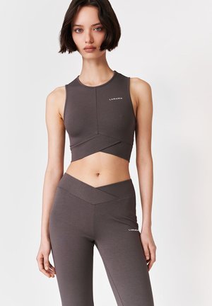 Kobieta z krótkimi ciemnymi włosami, ubrana w dopasowany, ciemnoszary bezrękawnik i wysokiej talii legginsy z logo "LAMANIA".