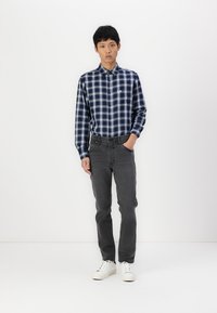 Navy blue checked shirt with button-down collar, paired with gray jeans and white sneakers, standing against a plain background.
