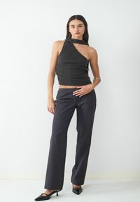 Zwarte mouwloze top met een asymmetrische halslijn en geknoopte details, gecombineerd met donker gestreepte, op maat gemaakte broek en punten schoenen.
