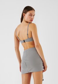 Črno-bela bikini zgornji del s tankimi naramnicami in zaponko; ujemajoča se visok Pas mini krilo z detajlom vezanja na strani.