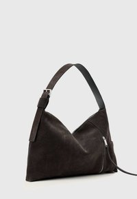 Mustast seemisnahast õlakott ühe reguleeritava rihmaga ja esiküljel nähtava diagonaalse luku, taust on ühevärviline.