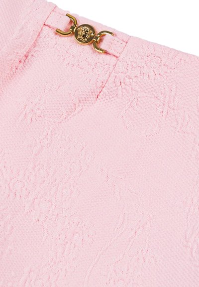 Tessuto rosa con una texture e motivi floreali, impreziosito da una chiusura con un emblema dorato. Vista ravvicinata che mette in risalto i dettagli della chiusura e del tessuto.