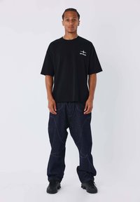Black cotton t-shirt with a small white logo, paired with oversized dark blue denim pants featuring visible stitching and a relaxed fit.