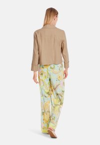 Tan cropped jacket with a collar, paired with light blue floral wide-leg pants featuring yellow, green, and pink patterns. Smooth texture.