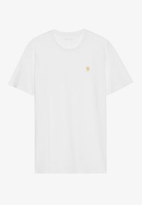 T-shirt en coton blanc à manches courtes, avec un col rond, affichant un petit emblème doré sur la poitrine gauche. Texture douce et coupe classique.